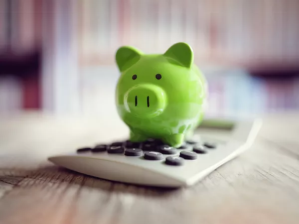 A green piggy bank sitting on a beige calculator.