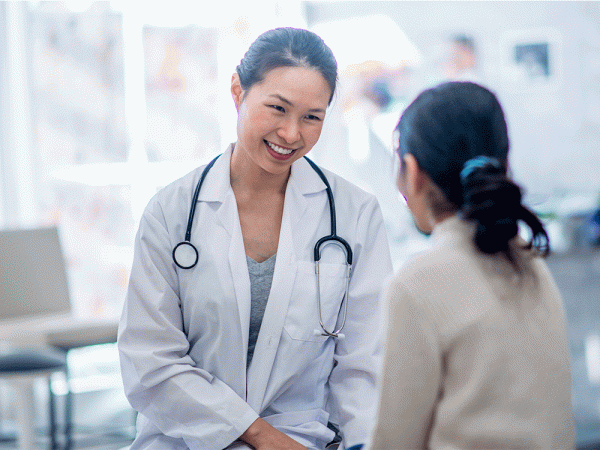 A doctor with a smile on her face sitting and speaking with a patient.