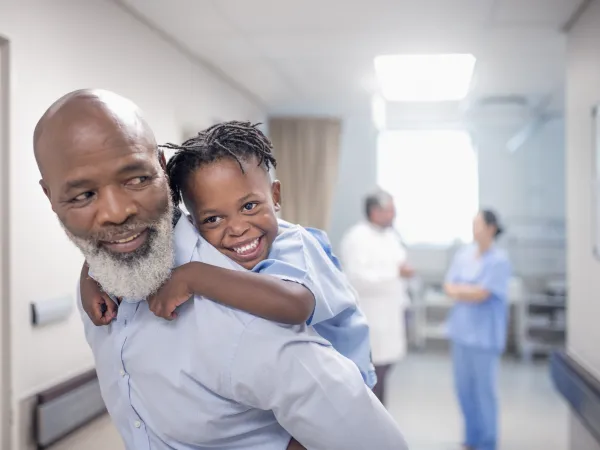 Man carrying child on back while doctors chat in background.
