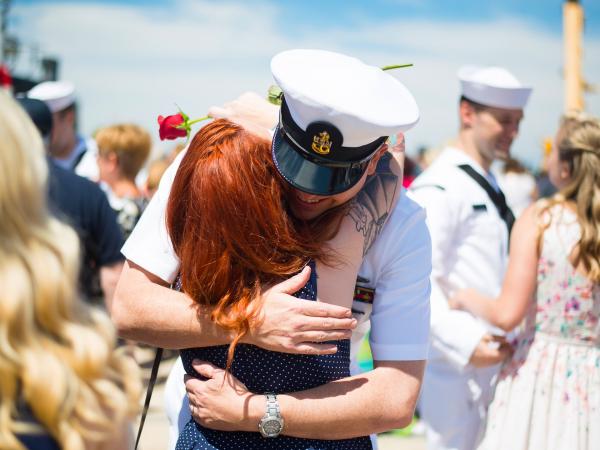 A navy officer hugging a woman with other soldiers and family greeting each other around them.