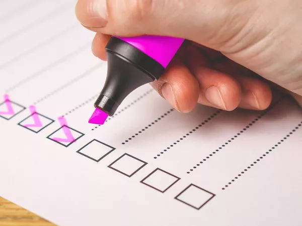 A hand checking off boxes on a document with pink marker.