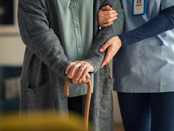 Nurse helping support a patient with a cane