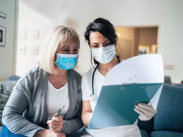 Doctor and patient wearing masks going over papers on a clipboard.