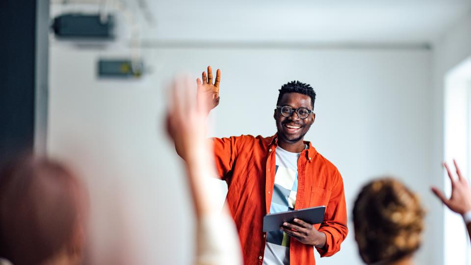 University staff smiles and holds tablet while asking students to raise their hands