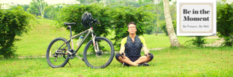 man sitting on ground, next to his bike, meditating