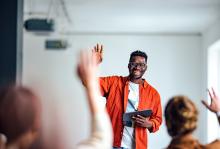 University teacher holds a tablet while asking students to raise their hands