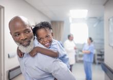 A parent piggybacks his child, with two healthcare professionals standing in the background.