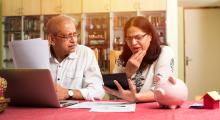 Senior South Asian couple doing home finance and checking bills with laptop, calculator and money while sitting at home