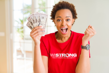 Excited woman holding up money in her right hand and wearing a WI Strong t-shirt.