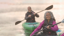 A woman kayaking with a man also kayaking behind her on her right.